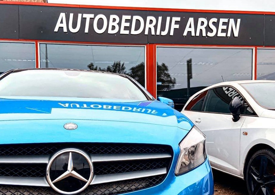 Een blauwe Mercedes A-klasse voor de zaak, met het naambord van Autobedrijf Arsen erachter