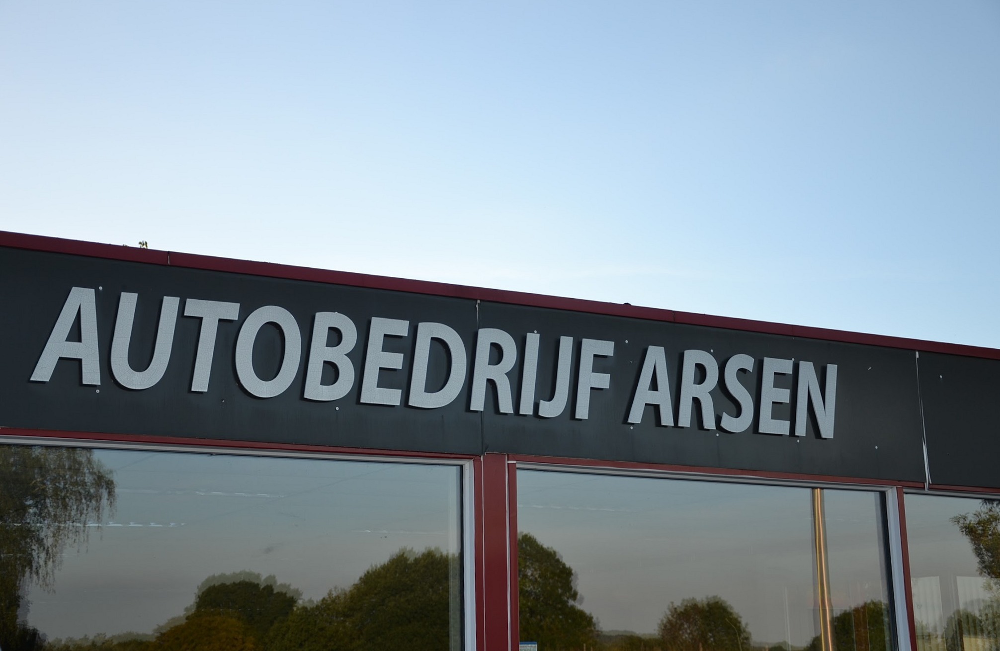 De gevel van Autobedrijf Arsen met de naam in grote letters onder een blauwe lucht